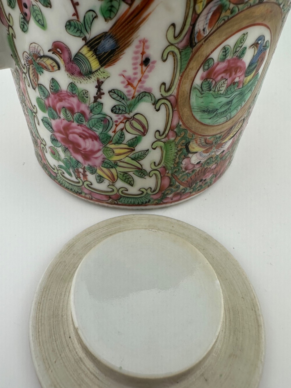 A Chinese Famille Rose cylindrical ceramic teapot with hand-painted court figures set beside its fitted woven wicker carrying case. View XV