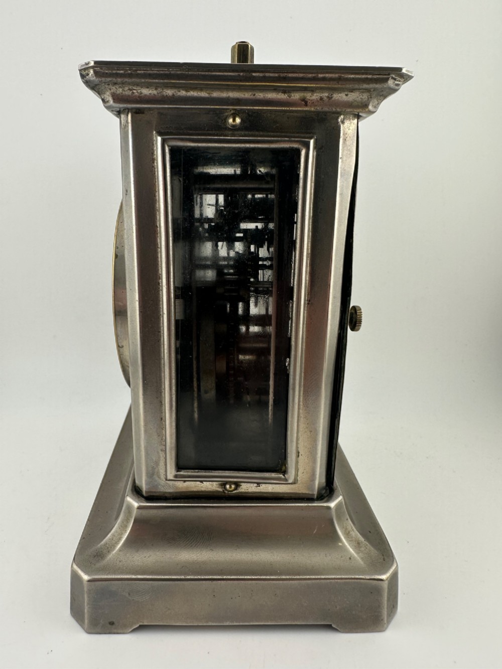 An Edwardian carriage clock with a silvered metal casing, brass carrying handle, and engraved brass mask around a white enamel dial. View VI