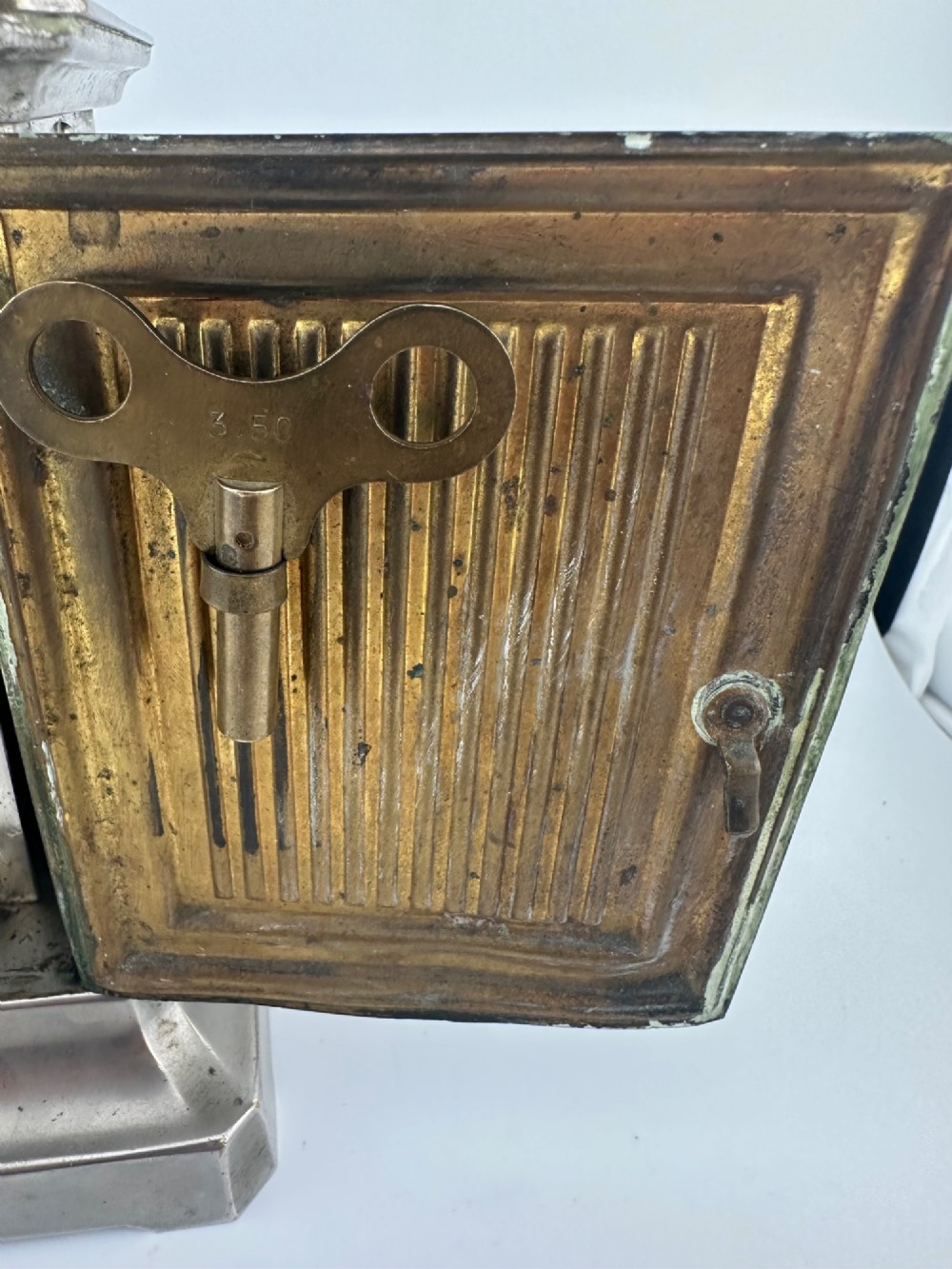 An Edwardian carriage clock with a silvered metal casing, brass carrying handle, and engraved brass mask around a white enamel dial. View IX
