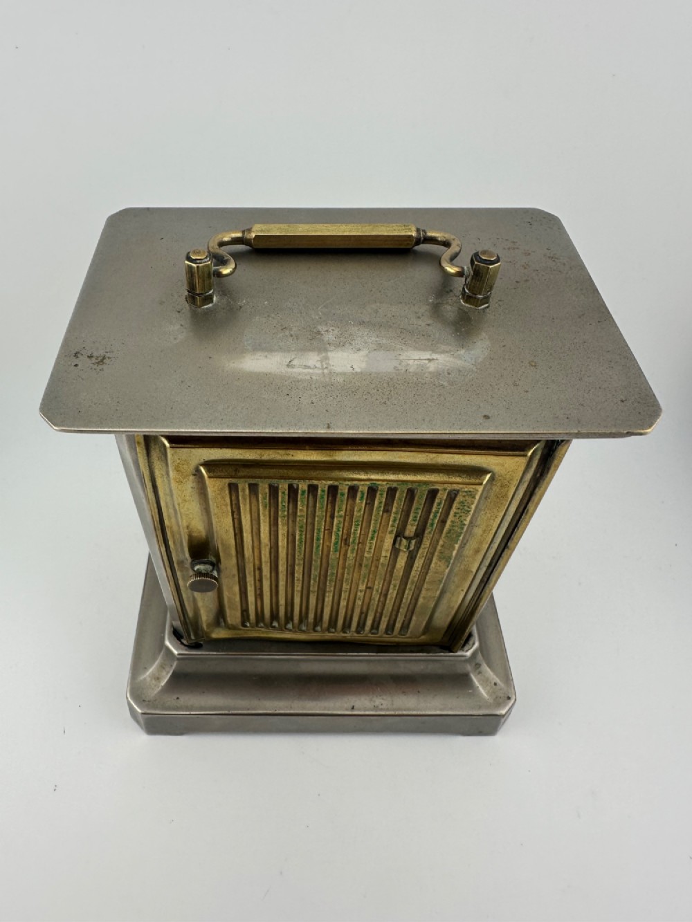 An Edwardian carriage clock with a silvered metal casing, brass carrying handle, and engraved brass mask around a white enamel dial. View X