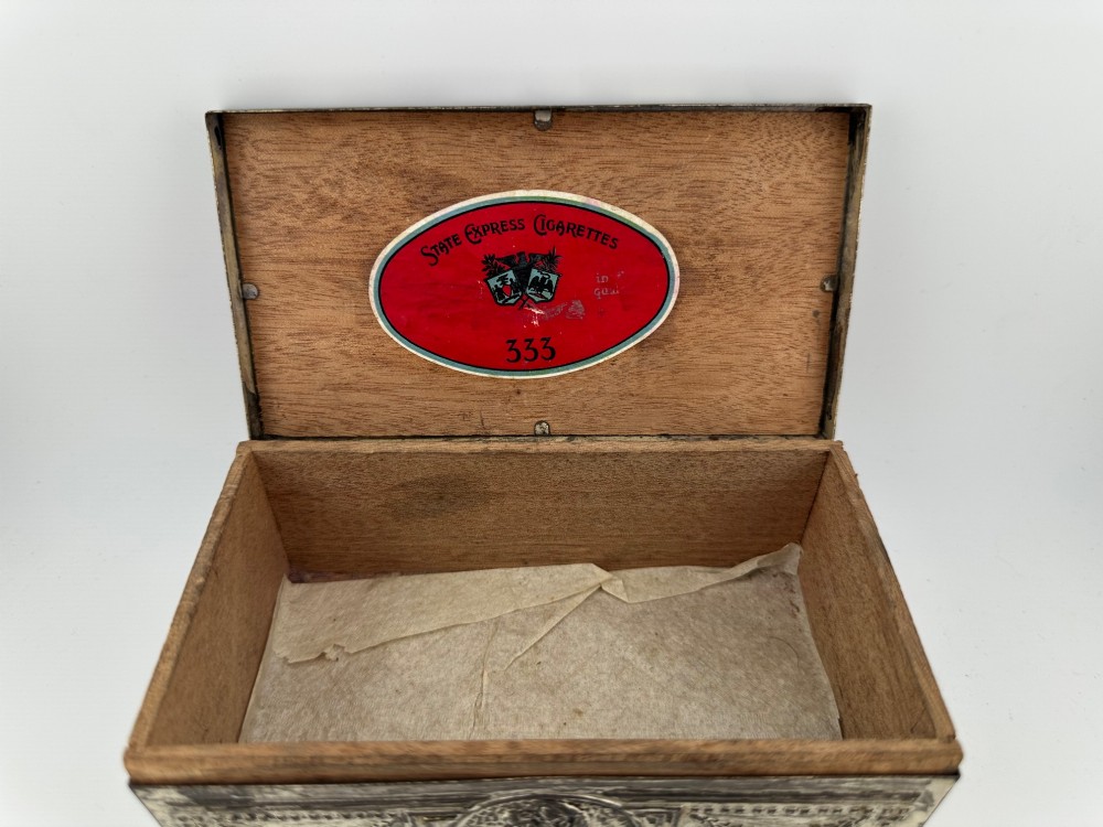 A rectangular silver-grey metal box featuring embossed neoclassical cherub medallions and relief swags across its hinged lid and sides. View VIII