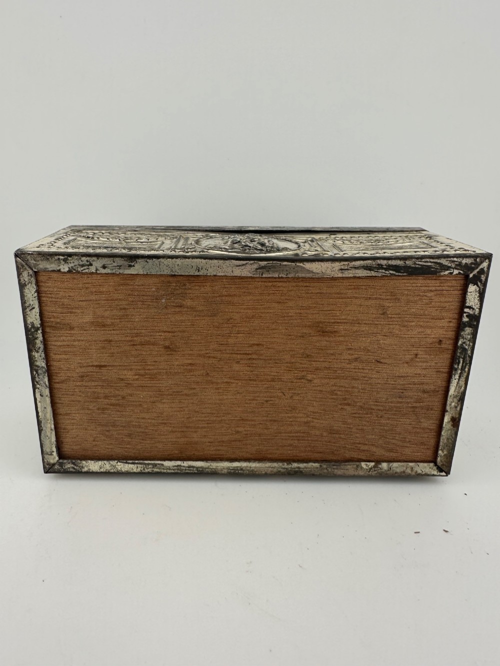 A rectangular silver-grey metal box featuring embossed neoclassical cherub medallions and relief swags across its hinged lid and sides. View IX
