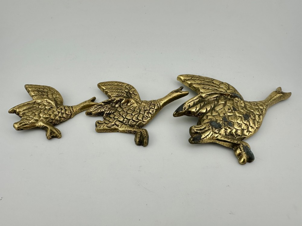 A set of three graduated cast brass flying geese wall plaques arranged by size with textured feather detailing. View II