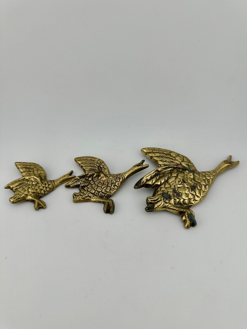 A set of three graduated cast brass flying geese wall plaques arranged by size with textured feather detailing.