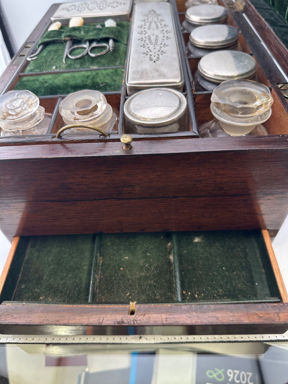 An open Victorian rosewood vanity box featuring a ruched green velvet lid lining, fitted interior compartments with silver-capped glass bottles, and a mother-of-pearl escutcheon. View III