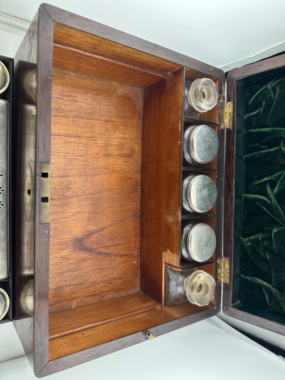 An open Victorian rosewood vanity box featuring a ruched green velvet lid lining, fitted interior compartments with silver-capped glass bottles, and a mother-of-pearl escutcheon. View V