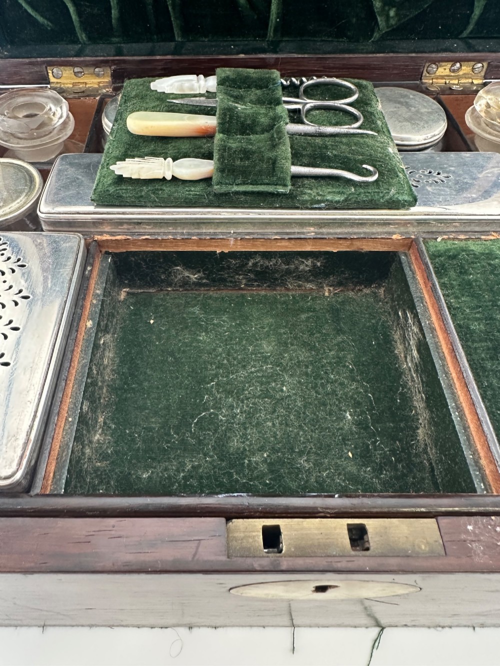 An open Victorian rosewood vanity box featuring a ruched green velvet lid lining, fitted interior compartments with silver-capped glass bottles, and a mother-of-pearl escutcheon. View XIV