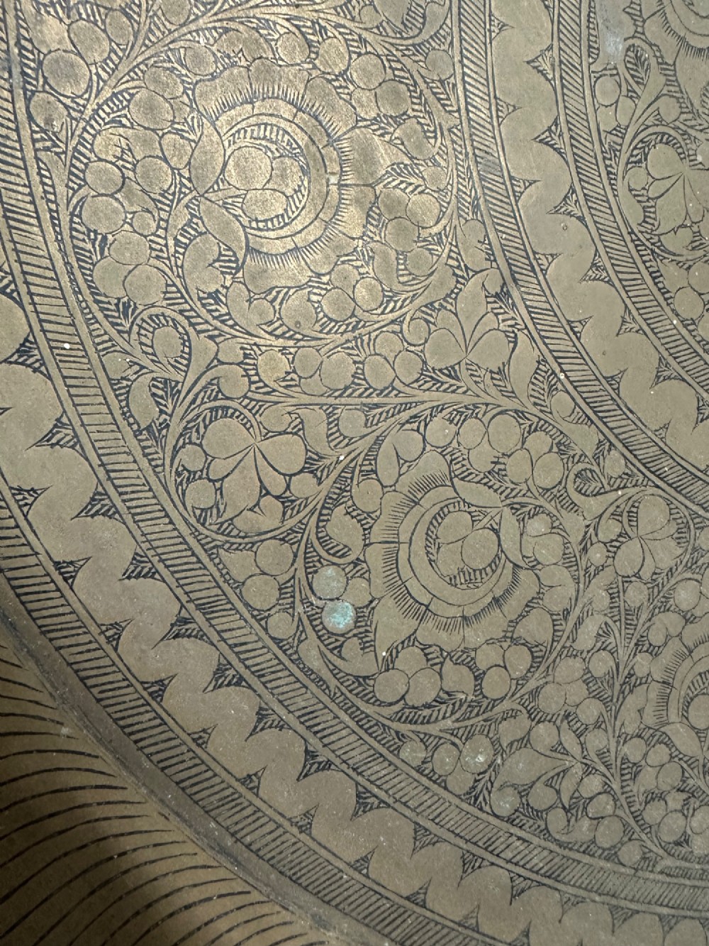 A large circular brass tray featuring intricate hand-engraved concentric floral and geometric patterns with a shallow rolled rim. View III