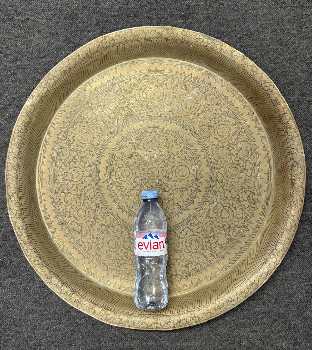 A large circular brass tray featuring intricate hand-engraved concentric floral and geometric patterns with a shallow rolled rim. View V