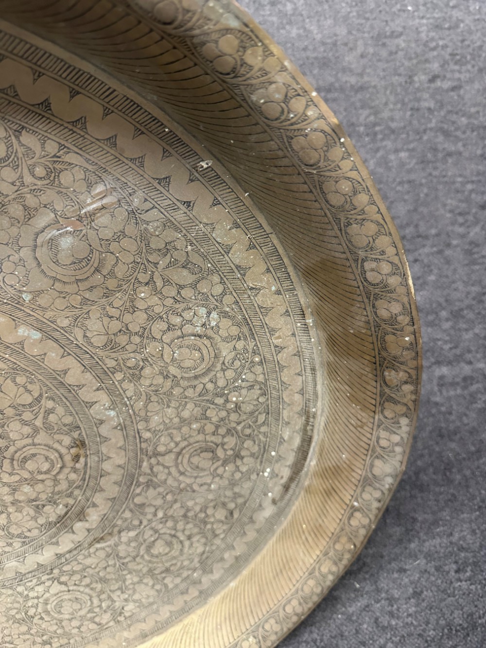 A large circular brass tray featuring intricate hand-engraved concentric floral and geometric patterns with a shallow rolled rim. View VII