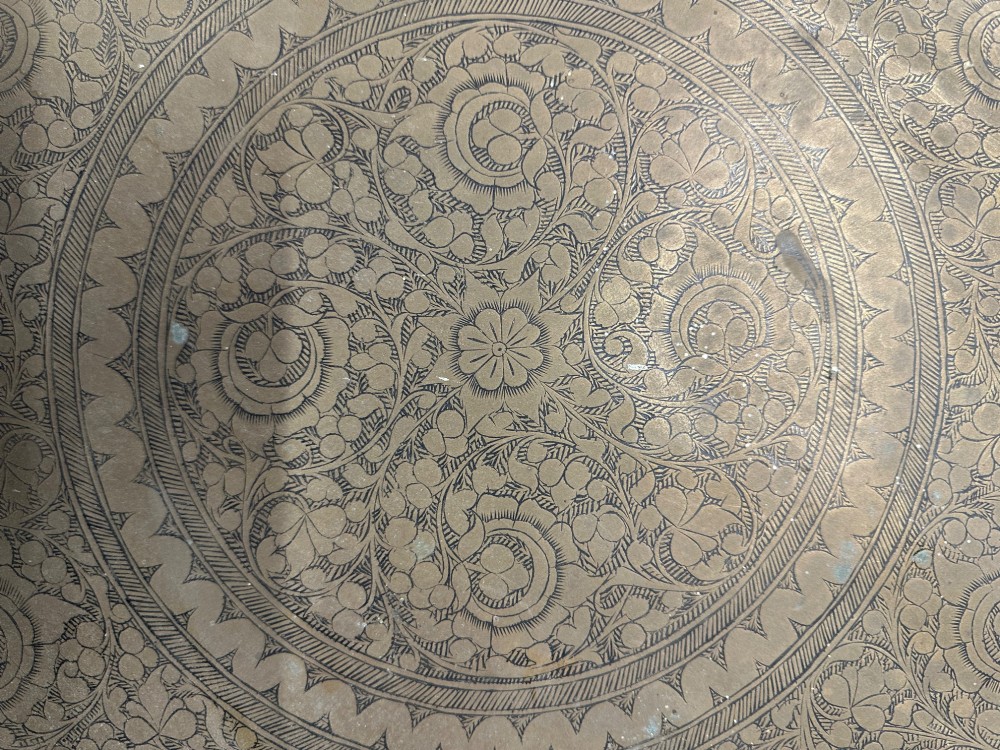 A large circular brass tray featuring intricate hand-engraved concentric floral and geometric patterns with a shallow rolled rim. View VIII
