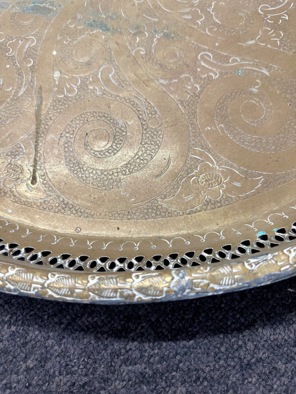 A circular antique brass tray featuring an intricately engraved swirling floral pattern and a pierced gallery rim. View X