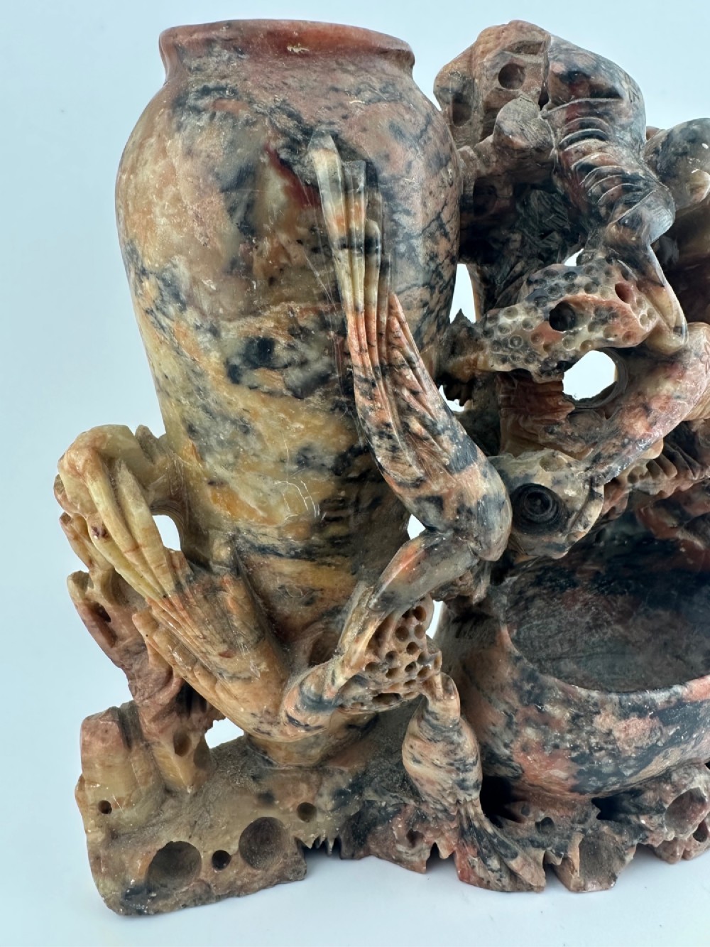 A Qing dynasty Chinese soapstone carving depicting a small vase, a shallow brush washer basin, and carved birds among naturalistic floral motifs in mottled red, grey, and cream stone. View II