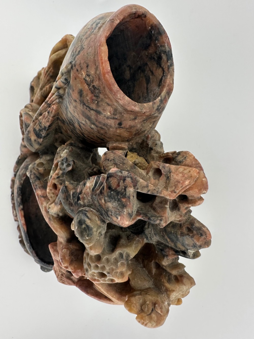 A Qing dynasty Chinese soapstone carving depicting a small vase, a shallow brush washer basin, and carved birds among naturalistic floral motifs in mottled red, grey, and cream stone. View IV