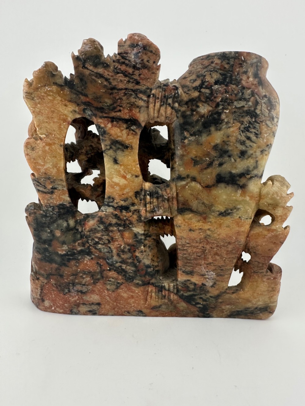 A Qing dynasty Chinese soapstone carving depicting a small vase, a shallow brush washer basin, and carved birds among naturalistic floral motifs in mottled red, grey, and cream stone. View V