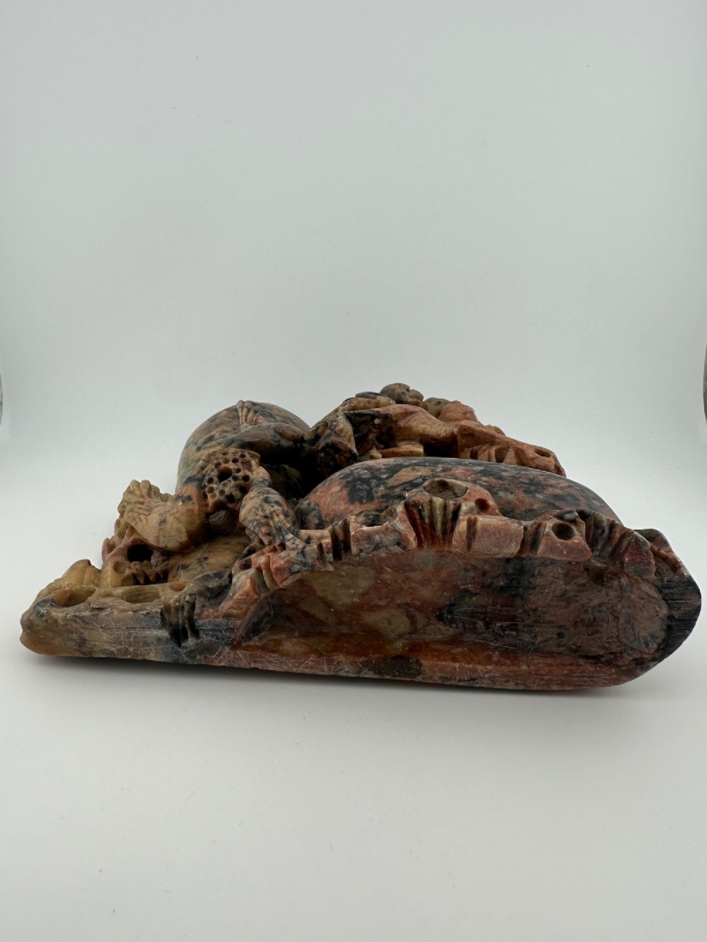 A Qing dynasty Chinese soapstone carving depicting a small vase, a shallow brush washer basin, and carved birds among naturalistic floral motifs in mottled red, grey, and cream stone. View VI