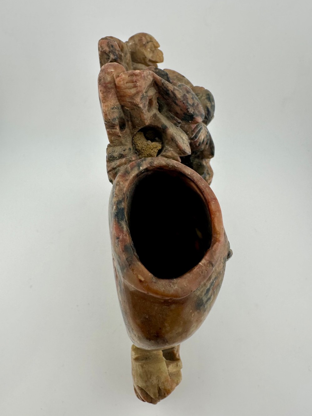 A Qing dynasty Chinese soapstone carving depicting a small vase, a shallow brush washer basin, and carved birds among naturalistic floral motifs in mottled red, grey, and cream stone. View VIII