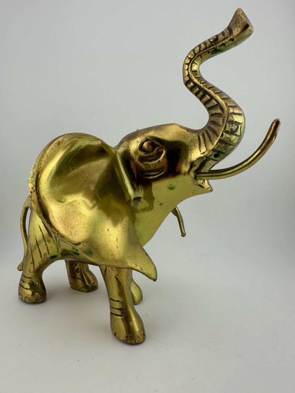 A solid cast brass elephant sculpture with an elevated raised trunk, detailed engraving along the body, and a polished gold finish. View II