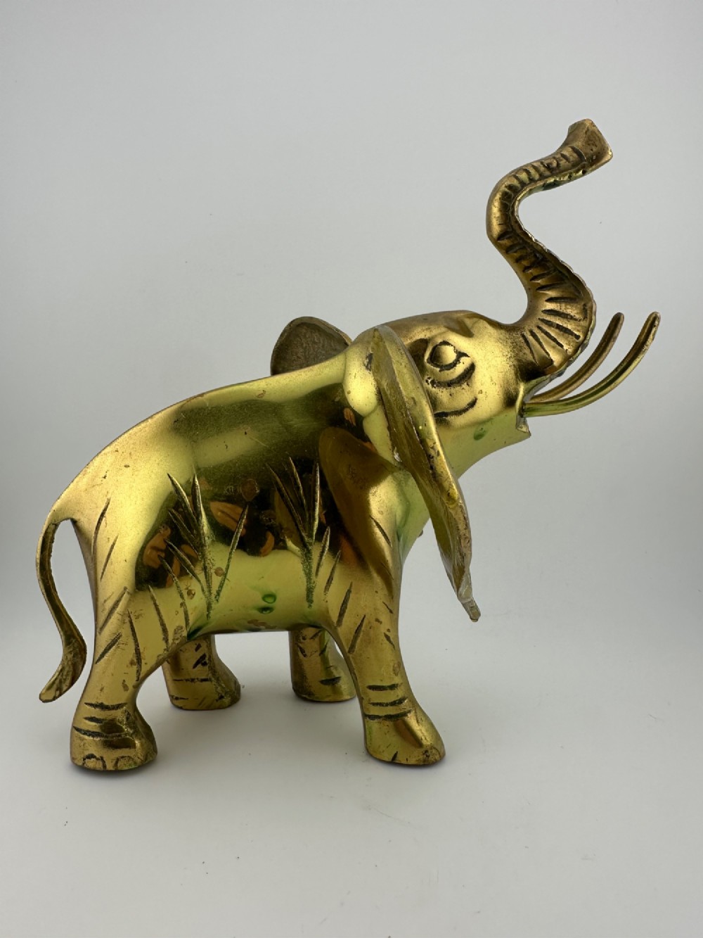 A solid cast brass elephant sculpture with an elevated raised trunk, detailed engraving along the body, and a polished gold finish. View III