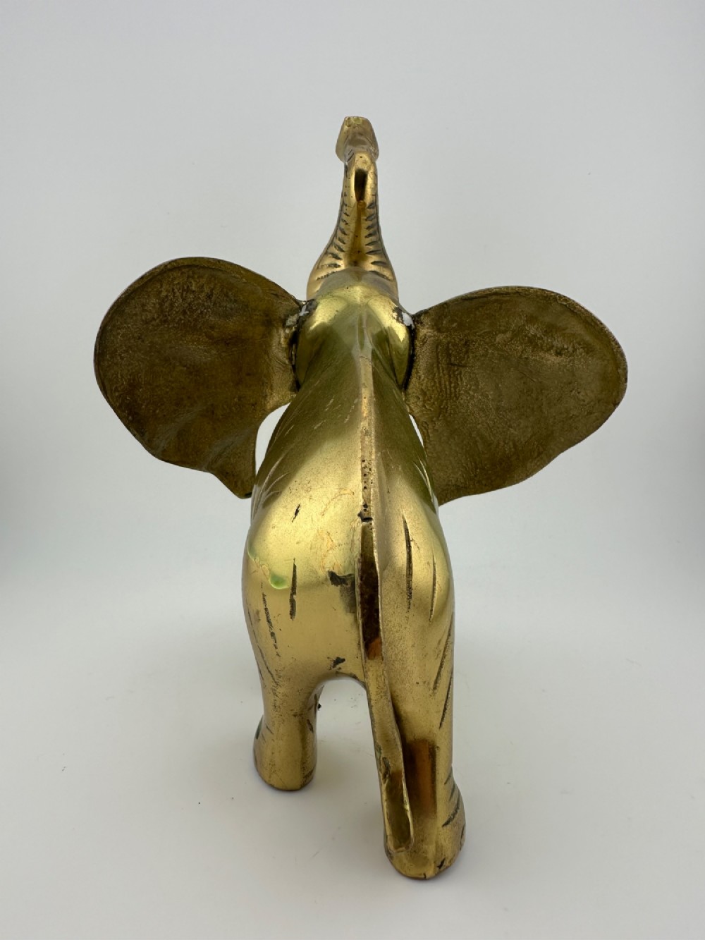 A solid cast brass elephant sculpture with an elevated raised trunk, detailed engraving along the body, and a polished gold finish. View IV