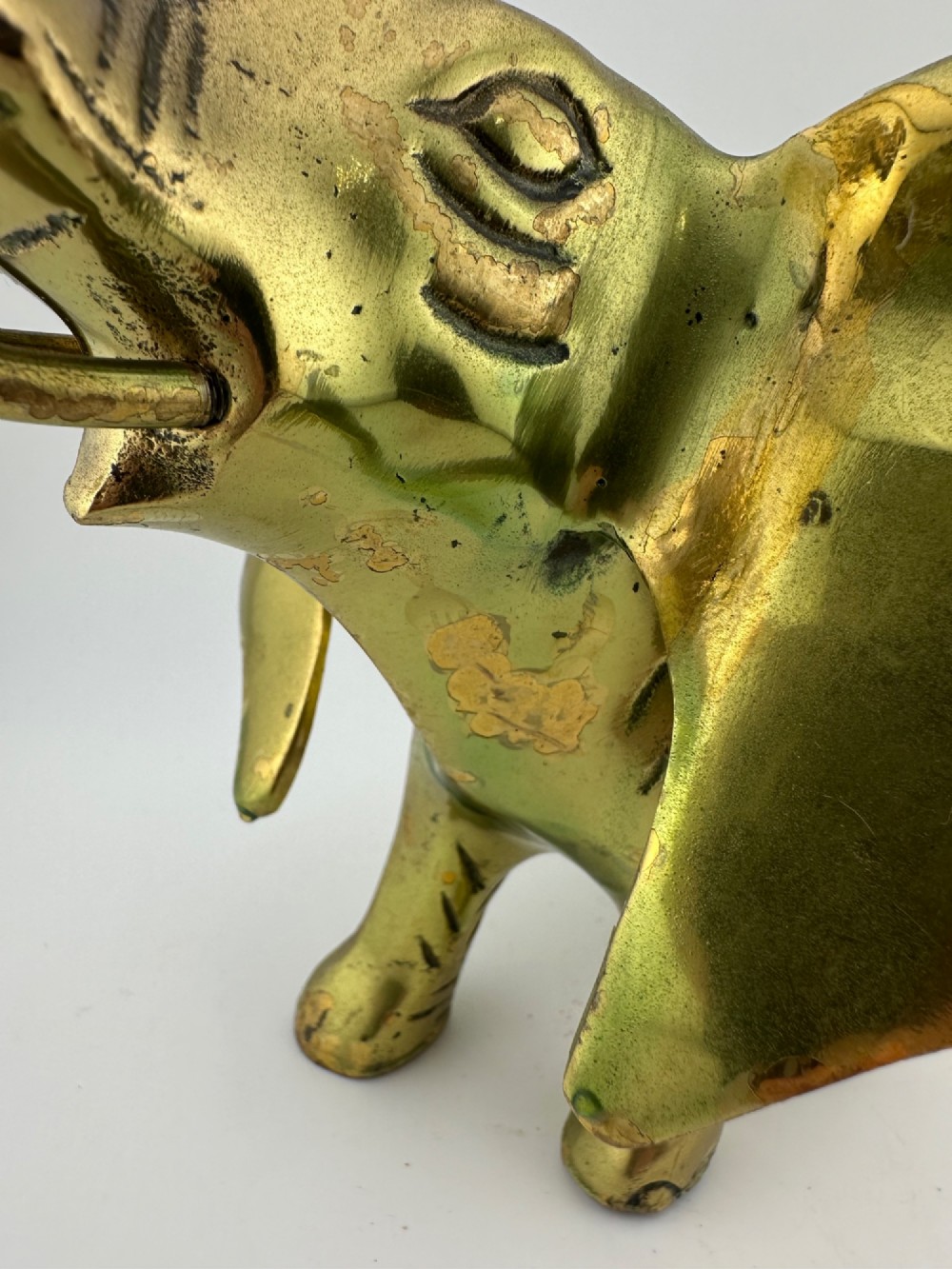 A solid cast brass elephant sculpture with an elevated raised trunk, detailed engraving along the body, and a polished gold finish. View VII