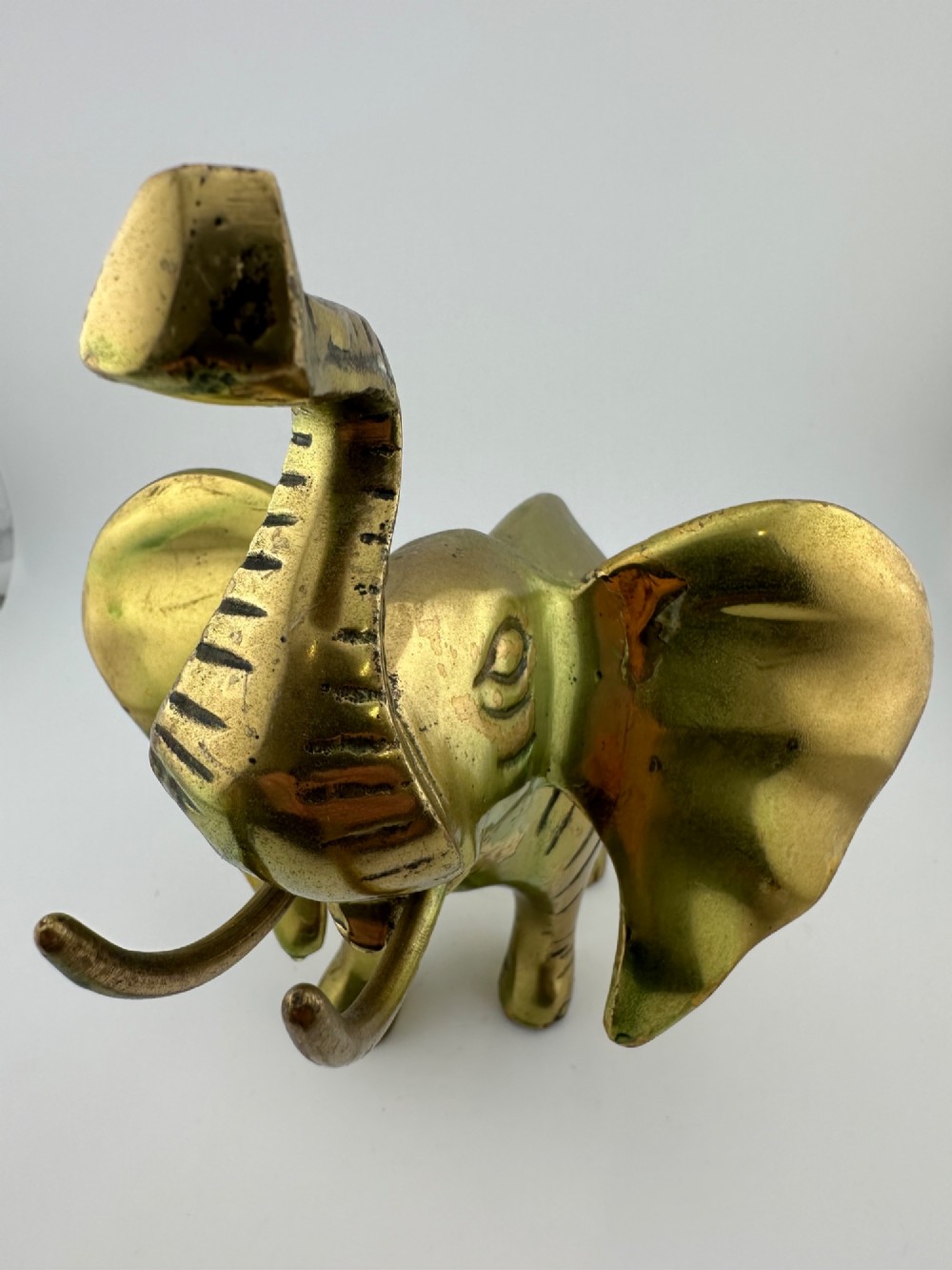 A solid cast brass elephant sculpture with an elevated raised trunk, detailed engraving along the body, and a polished gold finish. View IX