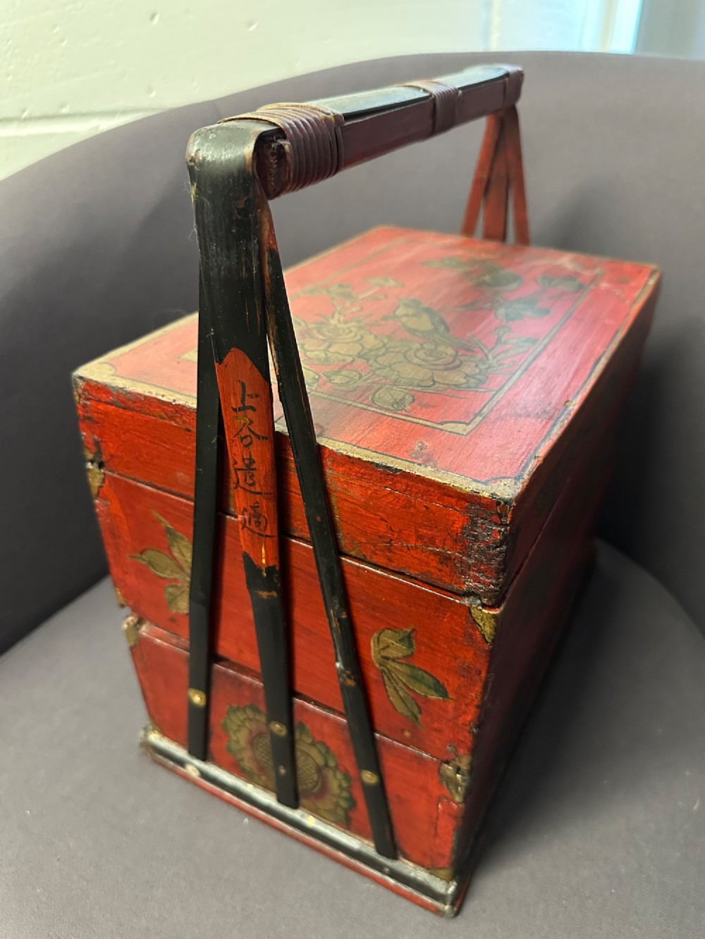 A three-tiered Chinese red lacquer wedding basket featuring hand-painted gold floral motifs and a black wooden carrying handle. View V