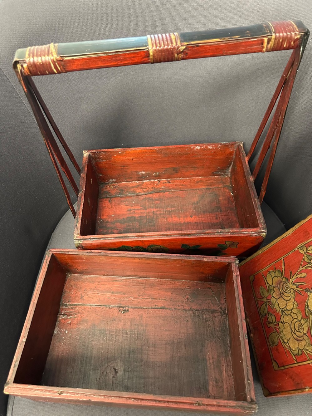 A three-tiered Chinese red lacquer wedding basket featuring hand-painted gold floral motifs and a black wooden carrying handle. View VI