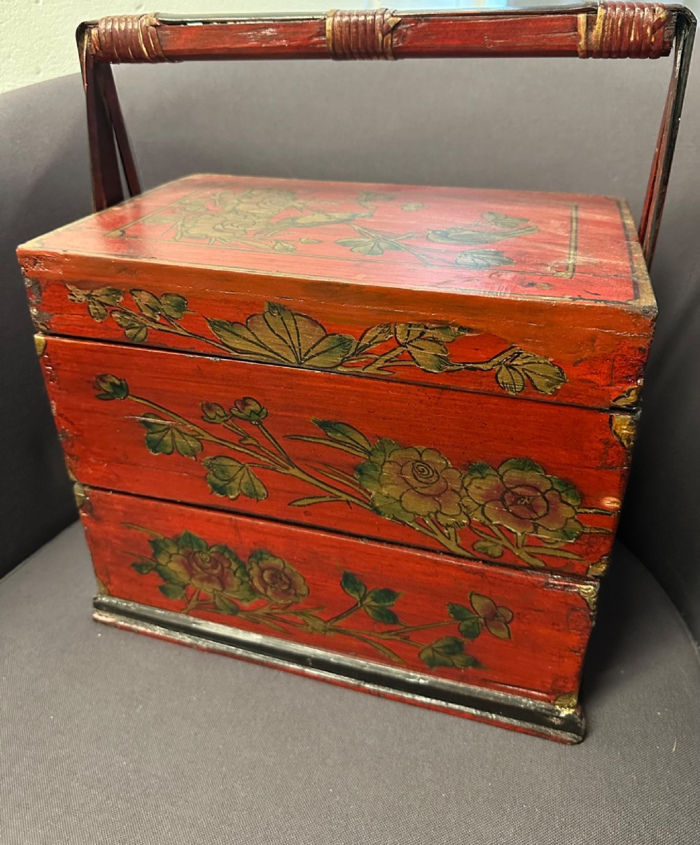 A three-tiered Chinese red lacquer wedding basket featuring hand-painted gold floral motifs and a black wooden carrying handle. View X