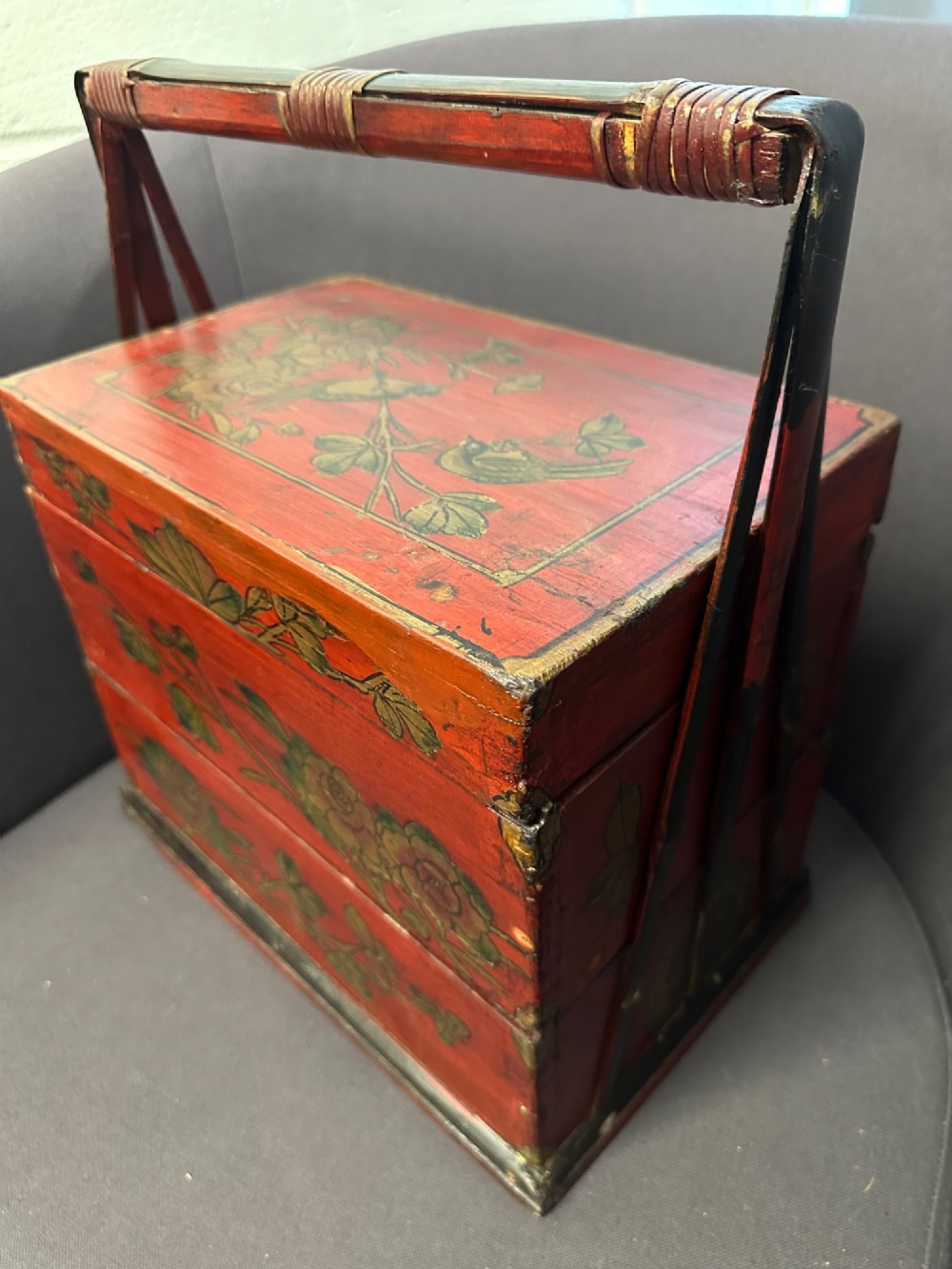 A three-tiered Chinese red lacquer wedding basket featuring hand-painted gold floral motifs and a black wooden carrying handle. View XV