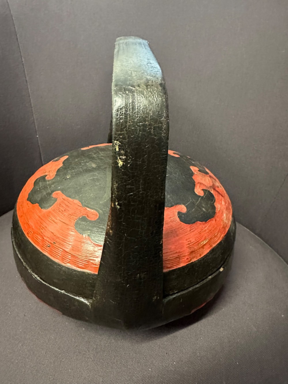 A traditional Chinese red and black lacquered rice basket featuring a high arched handle and painted decorative motifs on the lid. View V