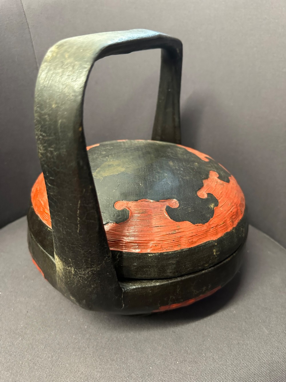 A traditional Chinese red and black lacquered rice basket featuring a high arched handle and painted decorative motifs on the lid. View VIII