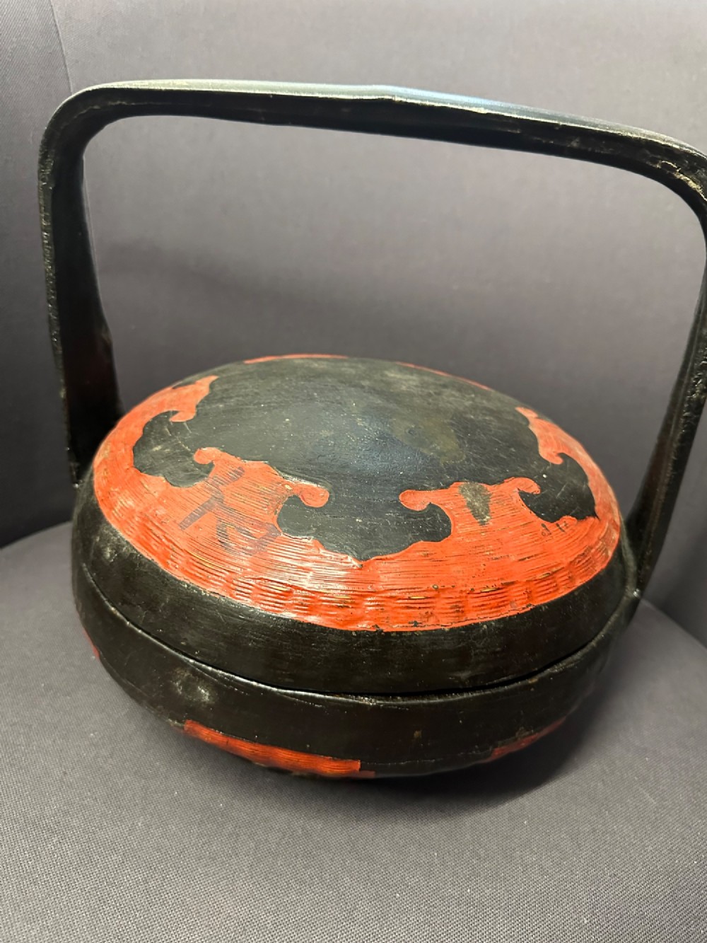 A traditional Chinese red and black lacquered rice basket featuring a high arched handle and painted decorative motifs on the lid. View XI