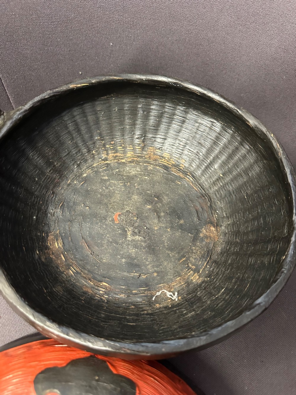 A traditional Chinese red and black lacquered rice basket featuring a high arched handle and painted decorative motifs on the lid. View XII