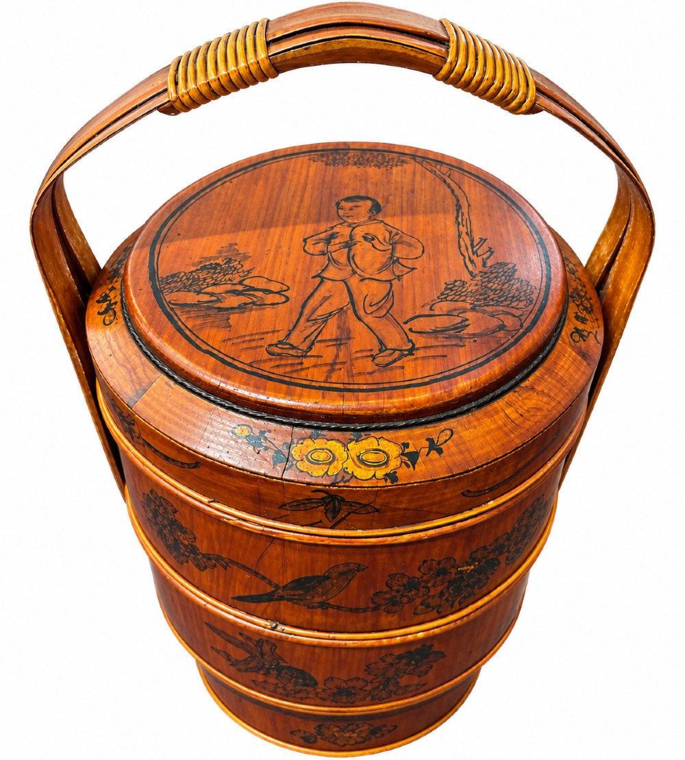 A late Qing Dynasty tiered Chinese food basket crafted from warm amber bamboo and wood, hand-painted with black line illustrations of a child on the lid and floral motifs around the body.