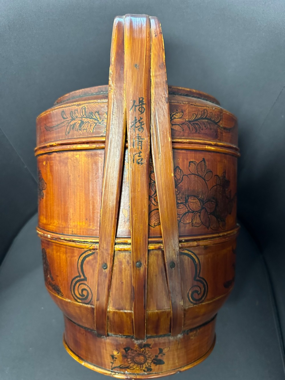 A late Qing Dynasty tiered Chinese food basket crafted from warm amber bamboo and wood, hand-painted with black line illustrations of a child on the lid and floral motifs around the body. View III