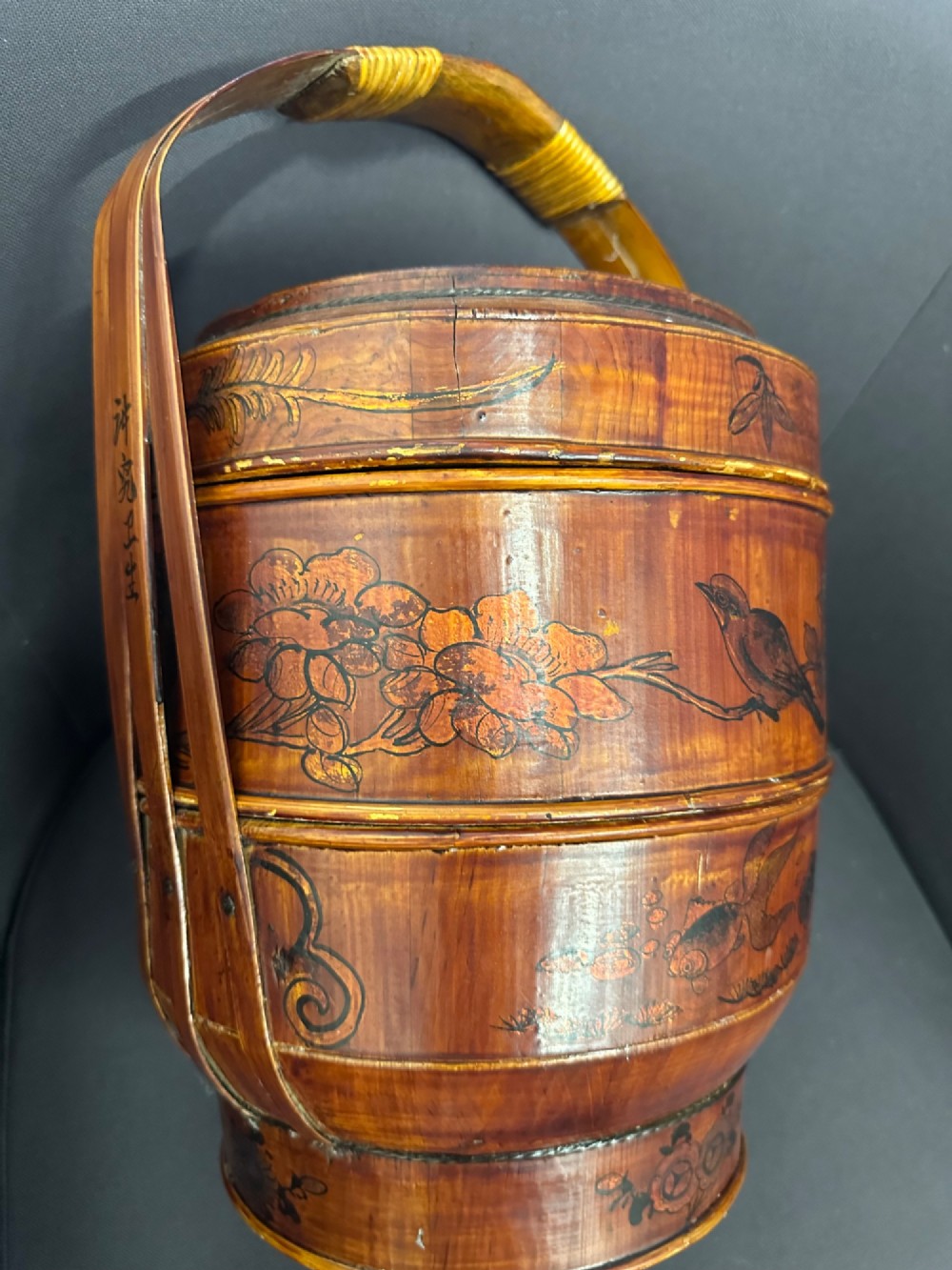A late Qing Dynasty tiered Chinese food basket crafted from warm amber bamboo and wood, hand-painted with black line illustrations of a child on the lid and floral motifs around the body. View V