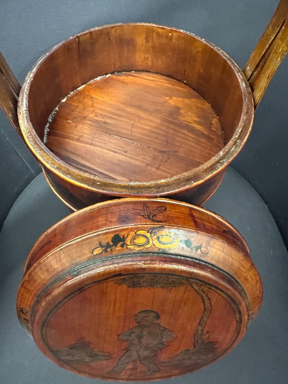 A late Qing Dynasty tiered Chinese food basket crafted from warm amber bamboo and wood, hand-painted with black line illustrations of a child on the lid and floral motifs around the body. View VIII
