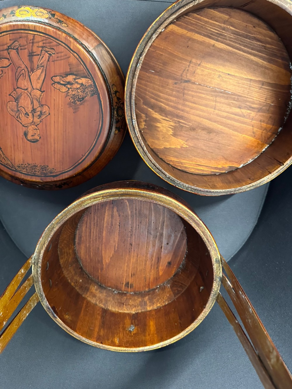 A late Qing Dynasty tiered Chinese food basket crafted from warm amber bamboo and wood, hand-painted with black line illustrations of a child on the lid and floral motifs around the body. View X
