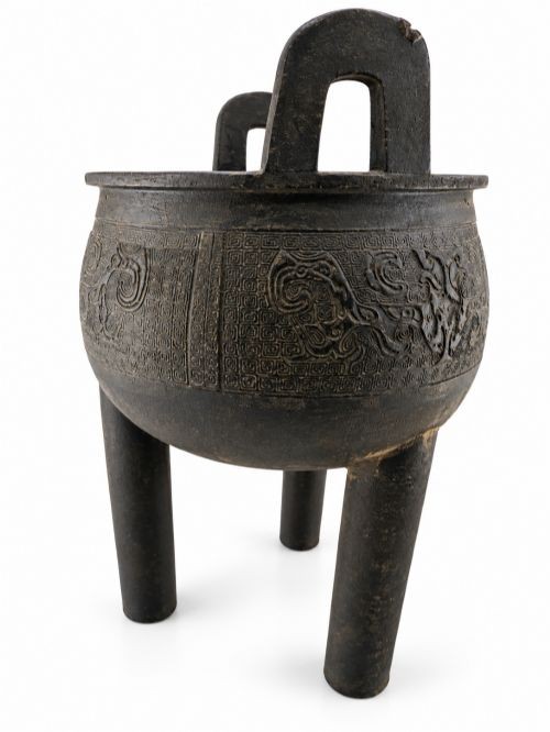 A dark patinated bronze tripod censer featuring upright loop handles and relief taotie mask carvings around the vessel body. View VII