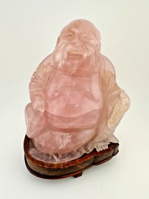 A carved pale pink rose quartz figure of a seated Laughing Buddha set upon a fitted carved dark hardwood base.