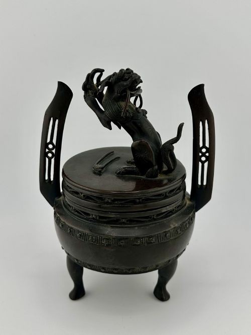 A dark patinated bronze tripod censer with a lid surmounted by a Qilin finial and featuring two tall pierced handles. View II