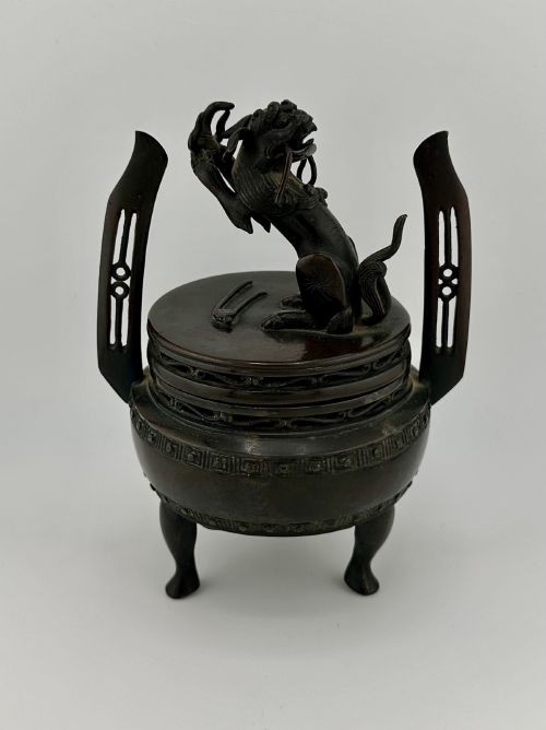 A dark patinated bronze tripod censer with a lid surmounted by a Qilin finial and featuring two tall pierced handles. View V