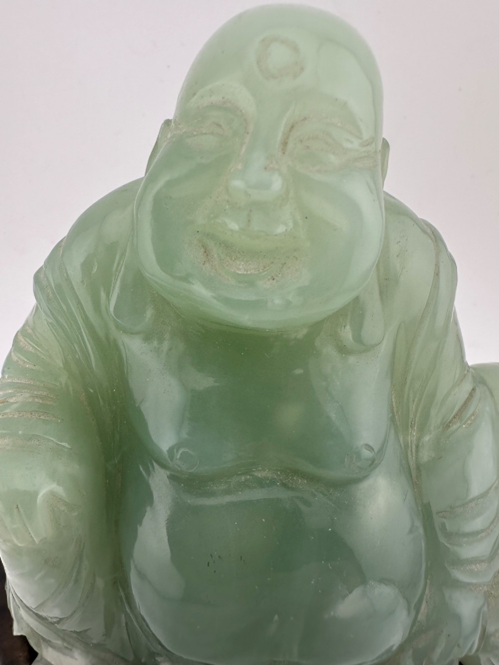 A hand-carved light green jadeite sculpture depicting a seated Laughing Buddha resting on a dark wooden fitted base. View III