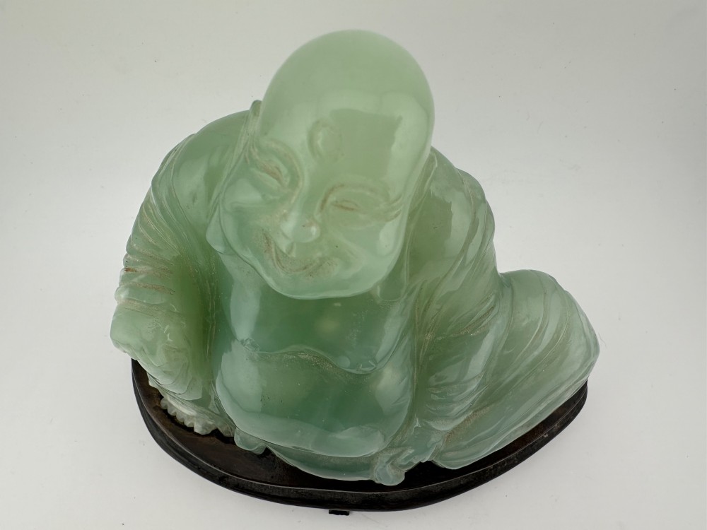 A hand-carved light green jadeite sculpture depicting a seated Laughing Buddha resting on a dark wooden fitted base. View VII