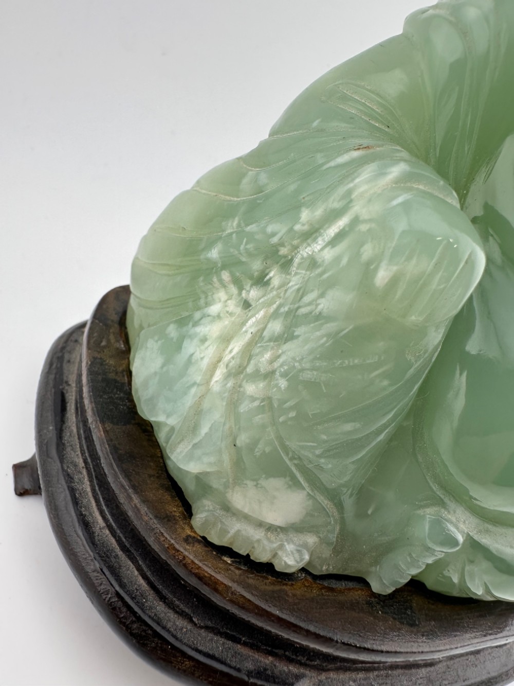 A hand-carved light green jadeite sculpture depicting a seated Laughing Buddha resting on a dark wooden fitted base. View XI