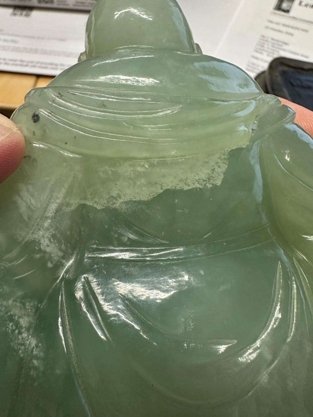 A hand-carved light green jadeite sculpture depicting a seated Laughing Buddha resting on a dark wooden fitted base. View XV
