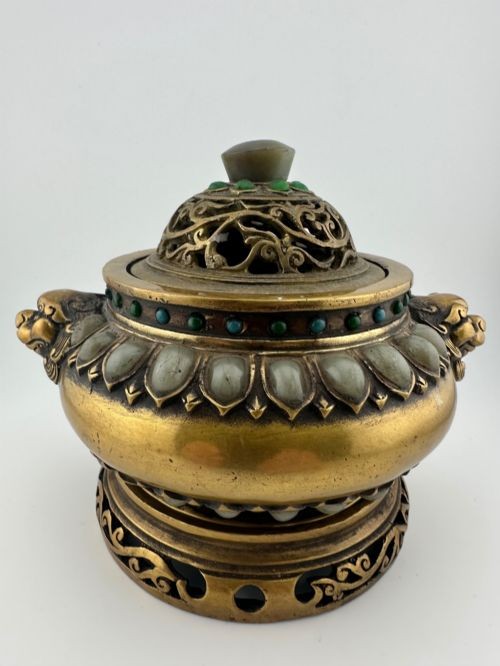 An antique cast bronze Chinese censer featuring a pierced cover, beast-head handles, inlaid green hardstone petals, and a matching fitted bronze stand.
