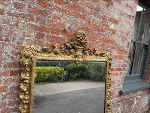 A large nineteenth-century carved giltwood overmantel mirror featuring a prominent central urn crest and floral mouldings. View II
