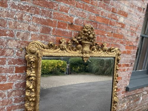 A large nineteenth-century carved giltwood overmantel mirror featuring a prominent central urn crest and floral mouldings. View IV